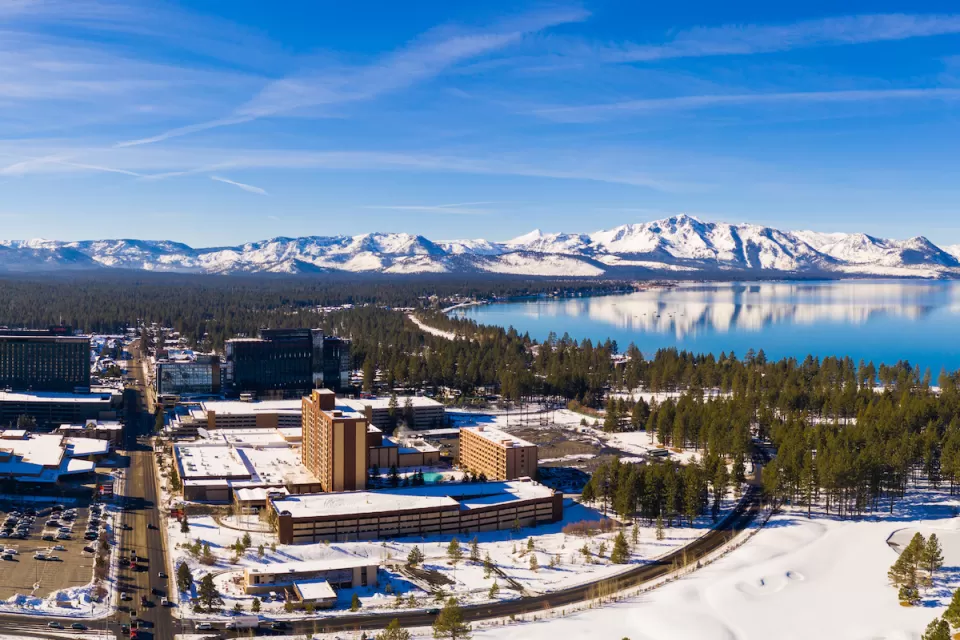 Aerial view of snowy town of Stateline, Nevada on shore of Lake tahoe with mountains in background.